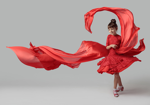 Dancing girl in a red dress with flying red fabric. Copy space.