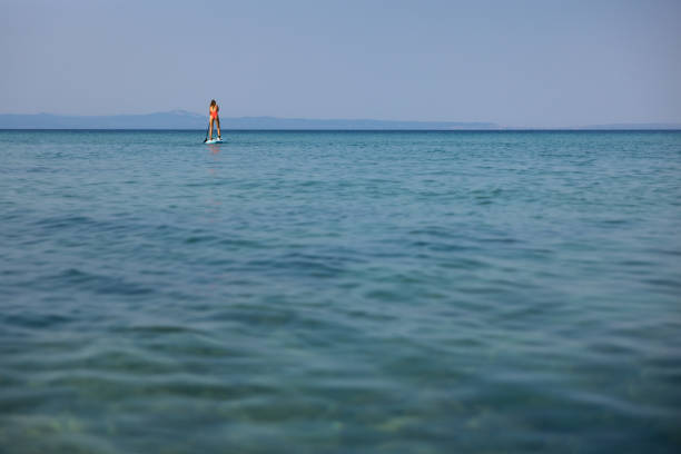 Young Caucasian woman in pink swimwear, enjoying the vacation while exploring sea with standup paddle board