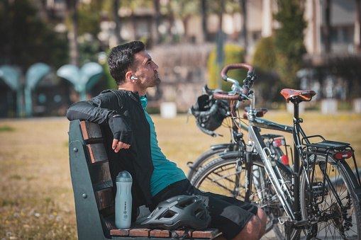 A young cyclist taking a break from cycling in the city park is resting on the bench