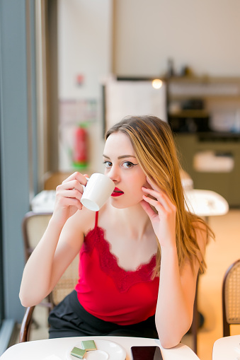 beautiful blonde woman drinking coffee in restaurant looking at camera