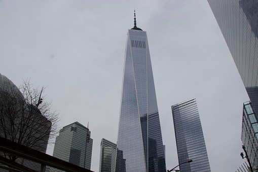 A ground view of the massively tall One World Trade Center and surrounding buildings on a cloudy Thursday afternoon.
