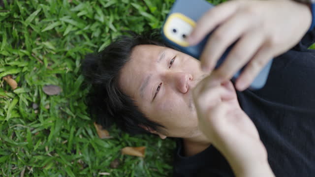 Asian male tourist napping on grass after checking his phone