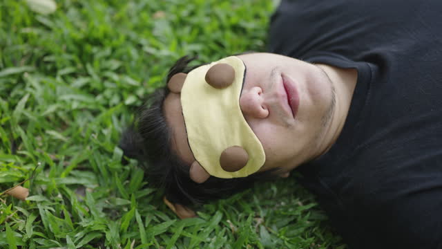 Asian man with blindfold sleeping on a grass field