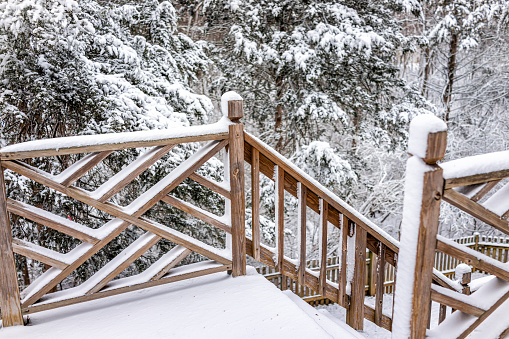 White snow covered outdoor home house wooden deck with railing fence in winter and steps going down to backyard and forest trees in northern Virginia