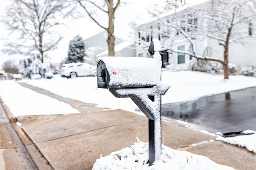 White snow covered mailbox on sidewalk street in northern Virginia suburbs and single family house in Washington DC metro area in winter season weather