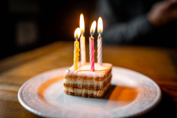 French Napolean cake slice macro closeup on white plate layered with cream and lit birthday candles on small pastry dessert and bokeh background