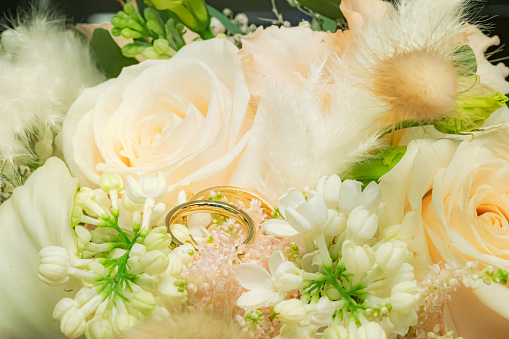 Gold wedding rings lying in green white wedding bouquet with fresh flowers