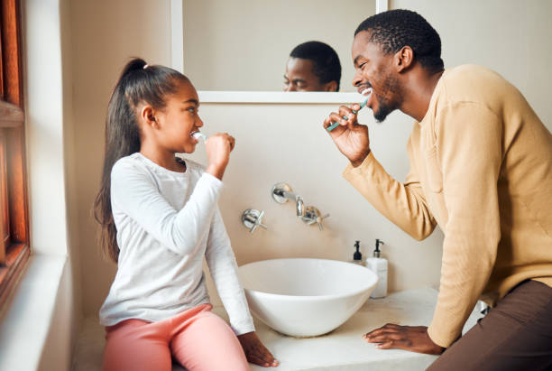 brushing teeth, dental health and father with daughter in a bathroom for hygiene, grooming and bonding. oral care, girl and parent, people and cleaning while having fun, playful and smile at home - offspring child toothy smile beautiful imagens e fotografias de stock