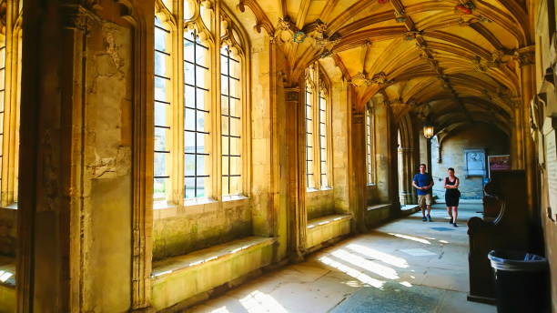 Christ Church, Oxford University, Oxford, United Kingdom - May 7, 2018: tourists walking in the Gothic corridor with curved ceiling and sunlight coming through before the pandemic