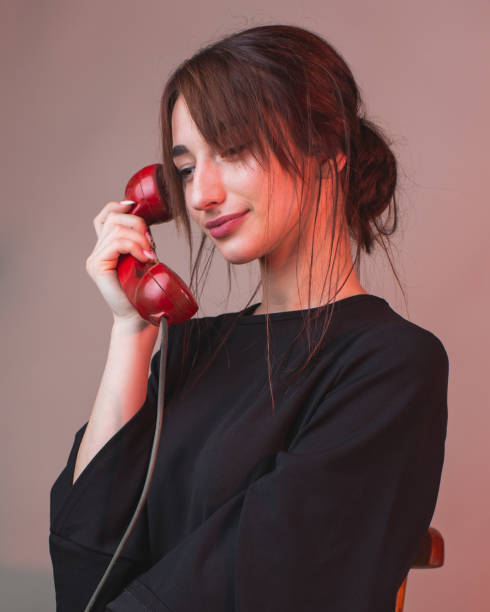 donna asiatica brunetta con ricevitore telefonico in mano dal telefono rotante in vestito nero in studio - surprise women humor old fashioned foto e immagini stock