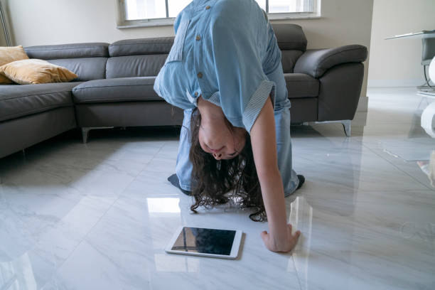 Young girl doing a handspring while watching digital table at home living room A young girl doing a handspring while watching a digital table that is on the floor of the home living room handspring stock pictures, royalty-free photos & images