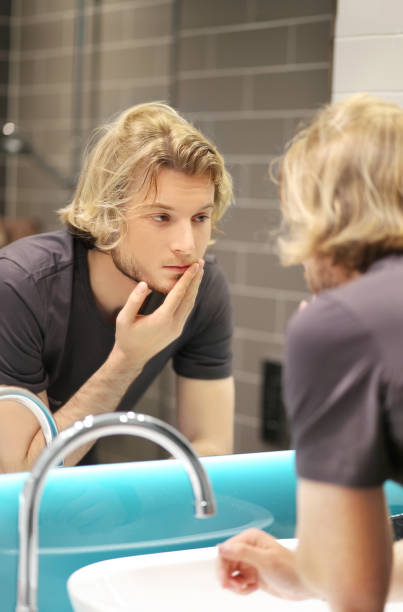 istock young man looking in the mirror,combing his hair,looking at problems on face 1474401342