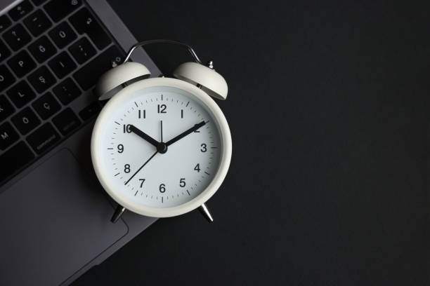 istock White alarm clock and laptop on black background 1474404629