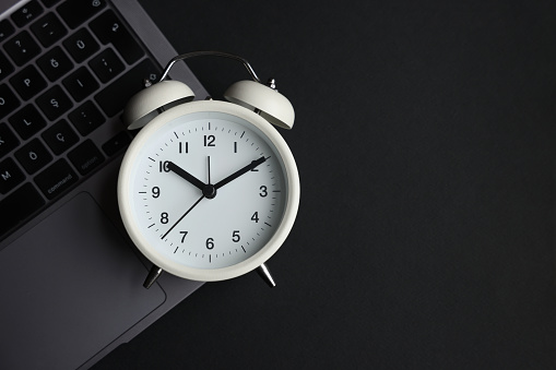 White alarm clock and laptop on black background