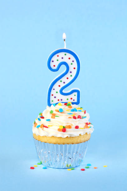 istock Iced birthday cupcake with with lit number 2 candle and sprinkles 1474408429
