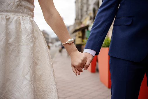 A bride and groom hold hands and walk down a street