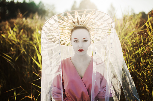 Asian woman in hat with red lips on background of high green grass.