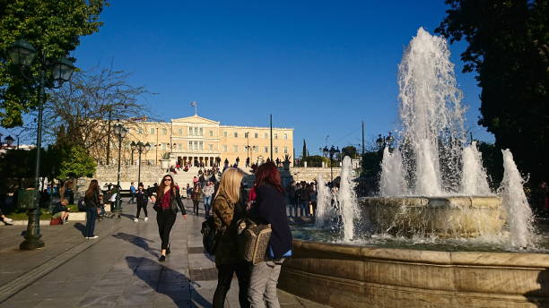 vue de la place syntagma avec les visiteurs passant devant la fontaine et le parlement hellénique en arrière-plan sous un ciel bleu clair au printemps avant la pandémie - syntagma square photos et images de collection
