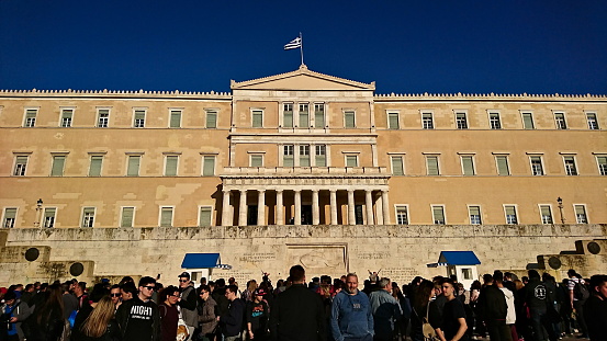 Athens, Greece - Mar 29, 2018: Tourists gather in front of the Hellenic Parliament to watch the guard mounting ceremony under a clear blue sky before the pandemic