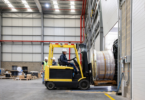Latin American employee working at a distribution warehouse and moving a cable drum with a forklift - trade concepts