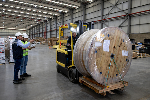 Foreperson supervising the shipping of a cable drum at a distribution warehouse and moving it with a forklift
