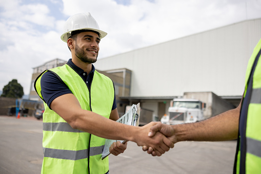 Happy foreperson greeting a coworker with a handshake at a distribution warehouse and smiling
