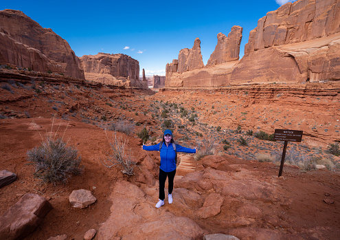 Happy woman with arms outstretched standing on top of the mountain. Arches National Park. Moab Utah, USA