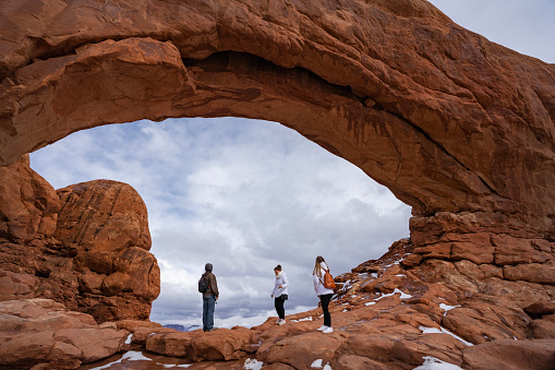 People exploring on winter vacation. People walking under North Window Arch on the Windows Loop Trail.  Arches National Park, Utah, USA.
