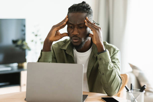 istock Upset black freelancer man sitting at workdesk at home office, working on laptop and suffering from headache 1474446965