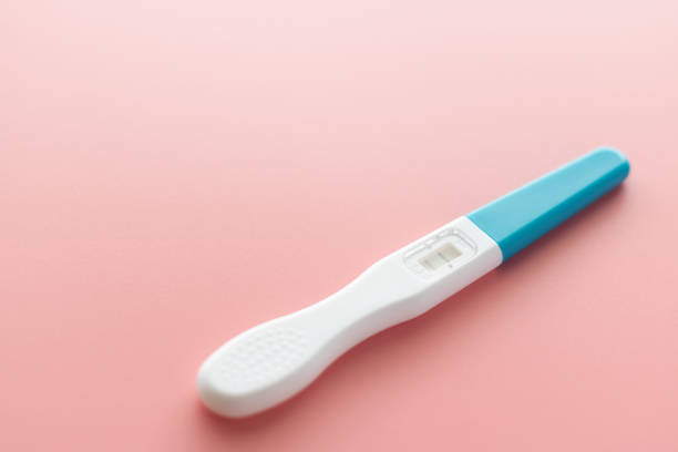 パステルの薄いピンクの背景に白いプラスチック妊娠検査陽性、2本の縞模様の結果。クローズ アップ。 - pregnancy test human pregnancy two objects isolated ストックフォトと画像