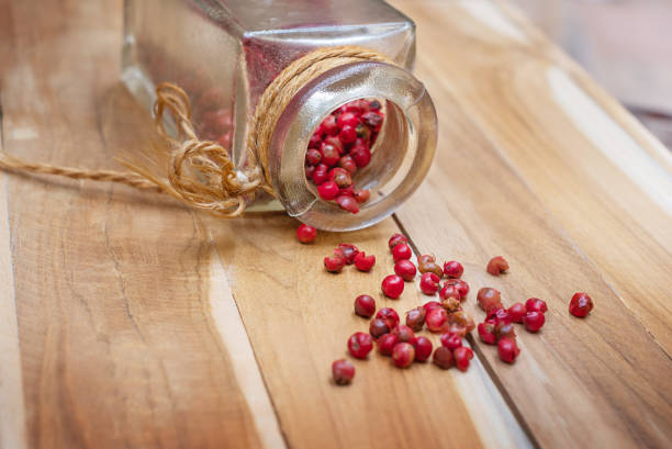 Pink pepper spilled out of a jar on a wooden surface