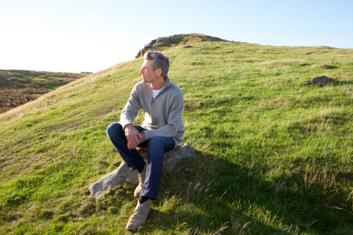 Man in countryside sitting on the side of hill looking off into the distance