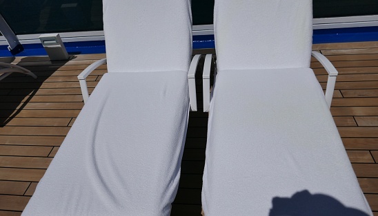 Side by side white chaise lounge chairs on wooden cruise ship deck