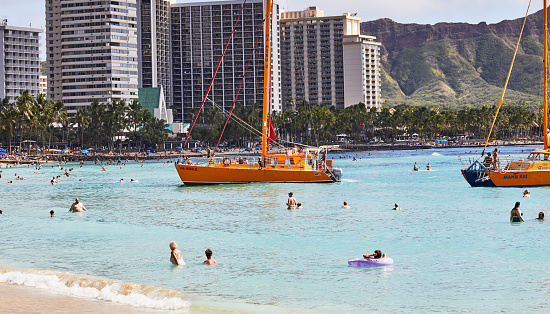 Waikiki, Oahu, Hawaii, USA, - February 6, 2023: People swimming and surfing in Waikiki with Tour Boats coming into Shore