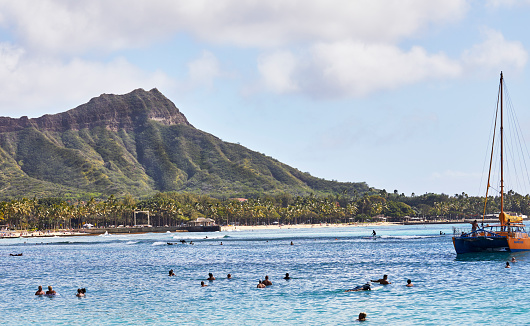 Waikiki, Oahu, Hawaii, USA, - February 6, 2023: People swimming and surfing in Waikiki with Diamond Head crater in the Background