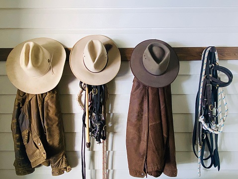 Horizontal still life of country and western style horse riding jacket and hat with bridles and ropes on wood wall hook and bench on rural farm horse property Bangalow NSW Australia