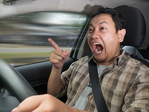 Portrait of Asian male driver mad of other car criver, speeding his car with anger dangerously,  mischievous reckless way of driving concept with motion blur