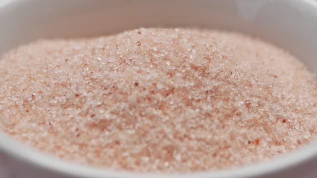 Raw whole dried pink Himalayan salt in a container on white