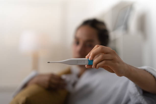 istock Young lady, checking her temperature on the thermometer she is holding in her hand. 1474488191