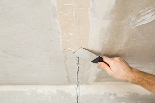 istock Young adult man hand using spatula and plastering concrete ceiling with putty on mesh in electric wire channel. Closeup. Repair work of home. Renovation process. 1474500563