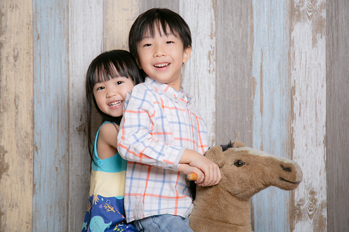 A boy and girl smile at the camera while riding a rocking horse. They look like they are having great fun.