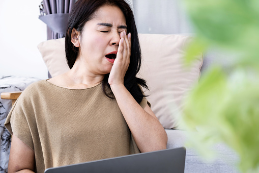 Tired Asian women feel sleepy and yawn while working on computer at home, lack of sleep, and chronic insomnia concept