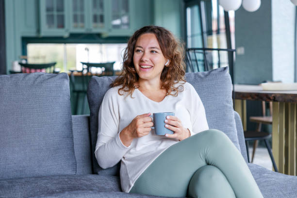 istock Young woman drinking cup of coffee sitting on sofa 1474505436