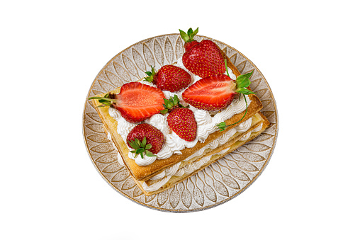 Puff pastry cake with whipped curd cream and fresh strawberries on a decorative plate isolated on white background