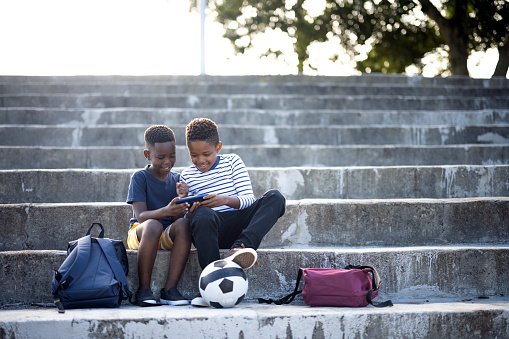 Young boys skipping school and using smart phone together in park