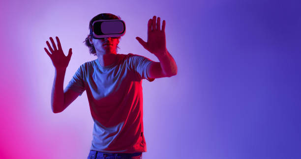 istock Amazing technology, entertainment, online game, study and virtual world in 3D simulation. Serious man in vr glasses plays and tries to touch something, in neon, studio shot, free space 1474511392