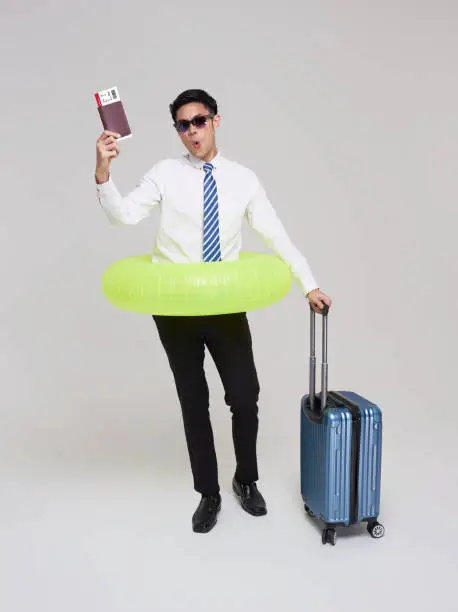Business travel summer time. Asian businessman showing air plane ticket with luggage and swim inflatable ring isolated on white background.