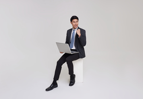 Business. Sucessful asian businessman working with laptop, using computer and smiling, sitting on white studio background.