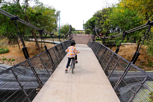 Elementary age child boy of Indian ethnicity riding a bicycle over the bridge