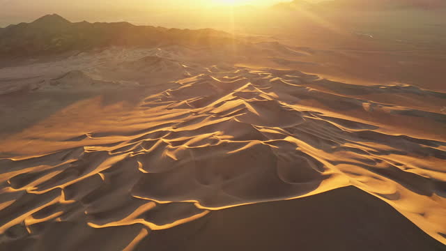 Desert sand dunes in golden light with arid mountain landscape in background